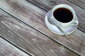 A cup of black coffee on a saucer with a spoon stands on a wooden table. Close-up.