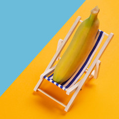 minimal concept of rest and summer, a banana lies in a lounge chair, on a yellow and blue background