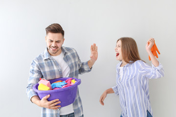 Angry wife scolding her husband with cleaning supplies on grey background