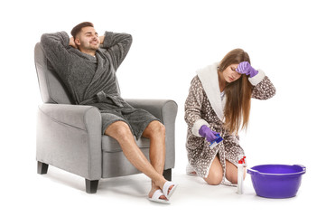Tired wife doing chores while her lazy husband sitting in armchair against white background