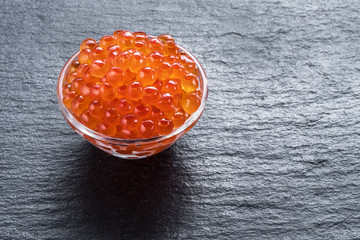 Red caviar in the bowl on gray graphite background.