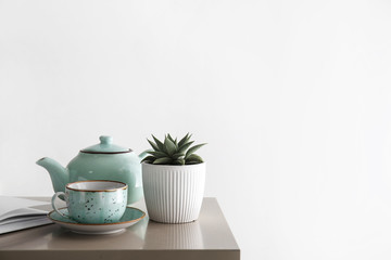 Succulent in pot with cup and teapot on table in room
