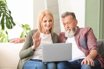Happy elderly couple with laptop resting at home