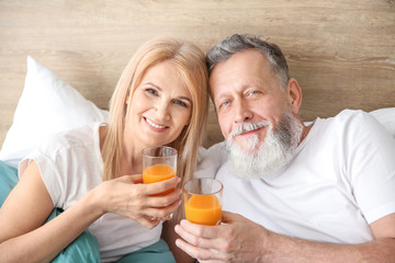 Happy elderly couple drinking juice in bed