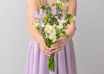 Woman with beautiful freesia flowers on light background
