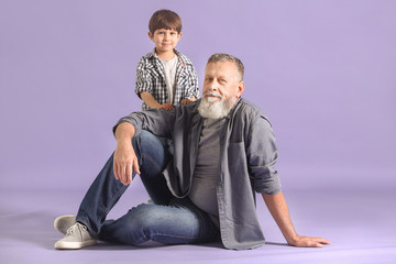Cute little boy with grandfather on color background