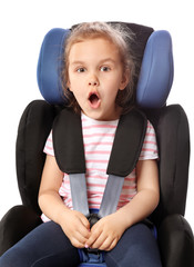Shocked little girl buckled in car safety seat against white background