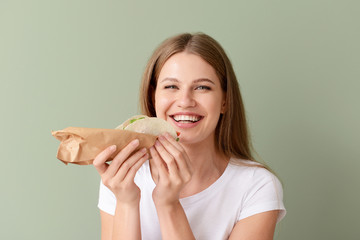 Woman eating tasty taco on color background