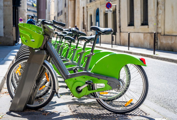 Green ecological electric bicycles with baskets for public rent stand in a row on a street of Paris waiting for cyclists