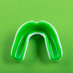 green rubber tooth protection for boxing lies on a green background, sport concept