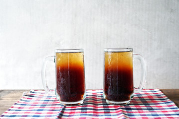 Two glasses of cool soft drink lay on cloth on the table with gray background.