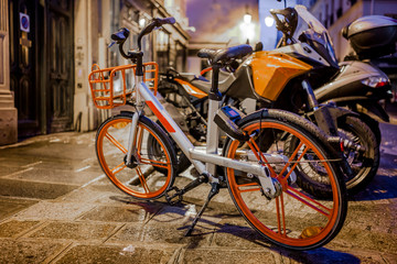 Naklejka na ściany i meble Rented wet from the rain bike with basket standing on the street of night sparkling lights Paris