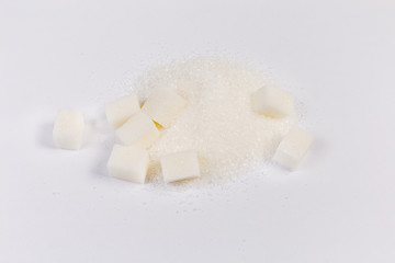 Handful of white sugar and sugar cubes on light surface