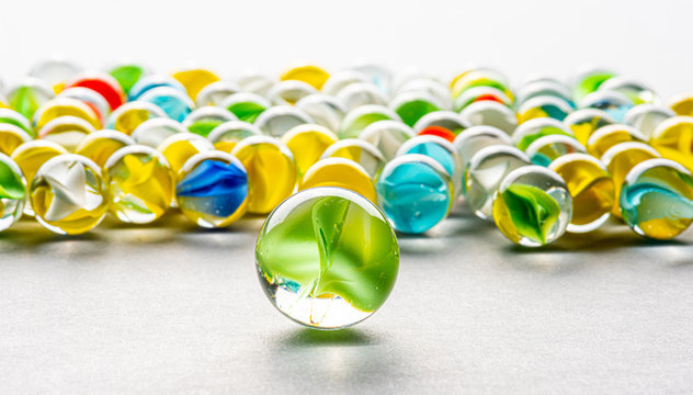 A big green glass marble  between yellow, green, blue and red marbles on a table.