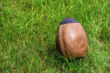 Old brown and black rugby ball on green grass