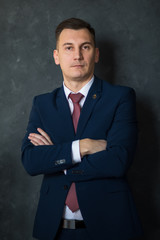 Portrait of young intelligent man lawyer standing with crossed arms in modern office building interior, successful male bank employee dressed in luxury suit posing with copy space area for your text