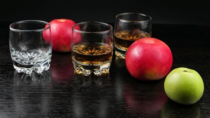 Glasses filled with whiskey on a dark wooden table with apples lying on it. Snack to complement for whiskey party