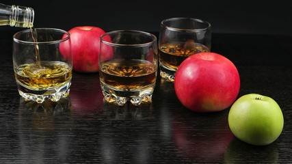 Glasses filled with whiskey on a dark wooden table with apples lying on it. Snack to complement for whiskey party