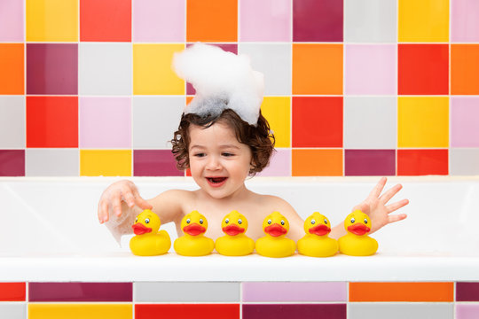 Smiling child in bathtub playing with rubber ducks