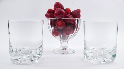 Glasses and glass bowl with strawberries on a white background
