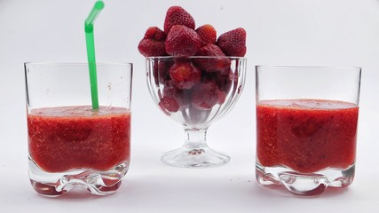 Glasses with strawberry smoothie and glass bowl with strawberries on a white background