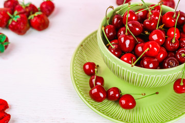 Bowl of fresh sweet cherries on a white wooden background, close up