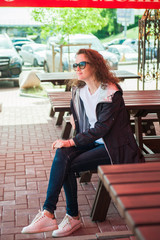 Outdoor portrait of a young beautiful curly woman in sunglasses posing on the street. Sunny day. City lifestyle.