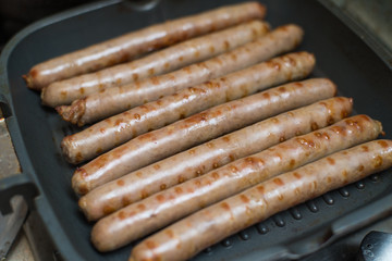 Meat sausages fried in a grill pan.