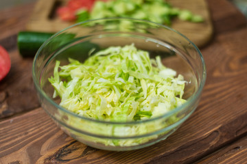 Chopped fresh green cabbage in a glass bowl on a wooden background. Cooking healthy, healthy, vegetable salad.