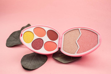 An open palette of egg-shaped eye shadows with warm-colored eye shadows and highlighters. on a pink background