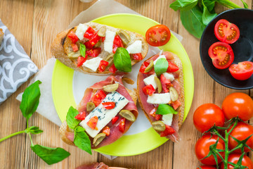 Traditional Italian bruschetta with blue cheese, feta, tomatoes, basil leaves, jamon on a wooden background.