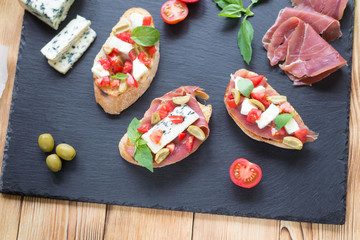 Traditional Italian bruschetta with blue cheese, feta, tomatoes, basil leaves, jamon on black stone background.