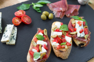 Traditional Italian bruschetta with blue cheese, feta, tomatoes, basil leaves, jamon on black stone background.