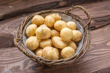 Raw fresh organic potatoes in a basket on a wooden background.