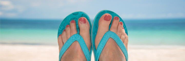 Woman bare sandy feet with blue flip flops, beach and sea in the background