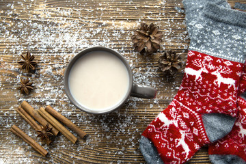 A Cup of hot spicy cocoa on brown wooden table. Red socks with christmas ornament and deer....