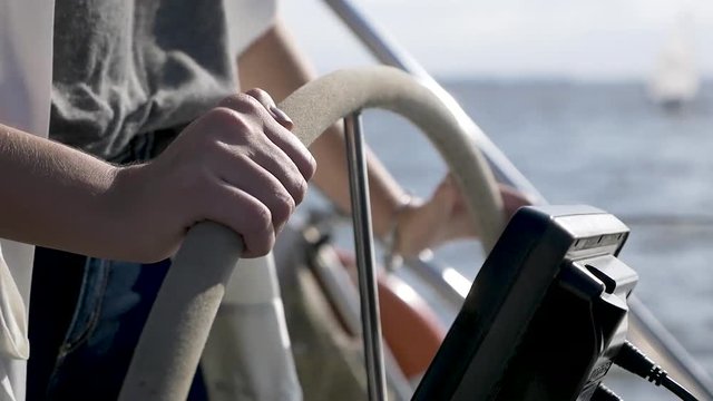 Female hands sailing a boat. She is wearing a dark gray T-shirt. The image is in a closer close-up and background blur