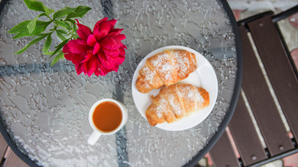 Two croissants on a plate next to a cup of cappuccino on a street table of a summer terrace cafe. Beautiful breakfast outdoor