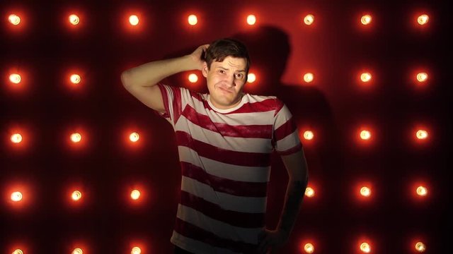 Upset man 30s on camera and scratching his head in perplexity over red background. Confused male Scratching Head. A confused young man is scratching his head