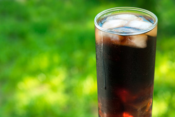 A glass of cola with ice and mint leaves against the background of fresh green grass. A concept for soft drinks.