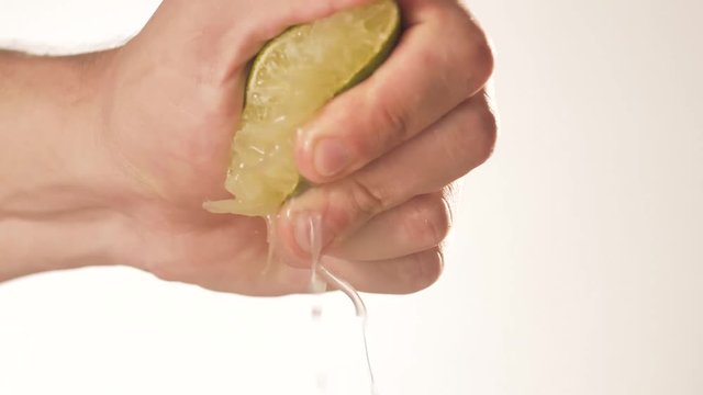 Male hands squeezing a green lemon. The image is in slow motion and closeup.