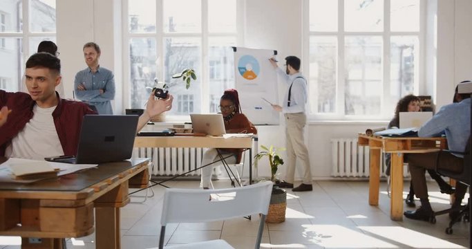 Camera moves left along modern loft office, happy multiethnic business people enjoy working at healthy trendy workplace.
