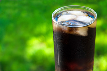 A glass of cola with ice and mint leaves against the background of fresh green grass. A concept for soft drinks.