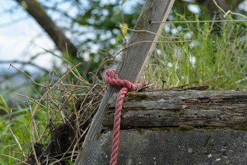 red rope hawser fixed and wrapped around a wooden doorpost green grass in background