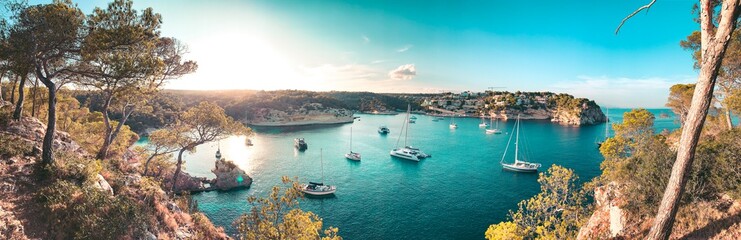 Panorama view of a beach bay with turquoise blue water and sailing boats and yachts at anchor with framed pine trees. Lovely romantic Cala Portals Vells, Mallorca, Spain. Balearic Islands