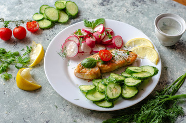 Salmon steak with lemon, tomatoes, cucumber and radish on a plate. Healthy seafood. Proper nutrition food.