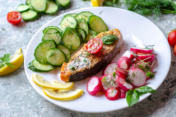 Salmon steak with lemon, tomatoes, cucumber and radish on a plate. Healthy seafood. Proper nutrition food.