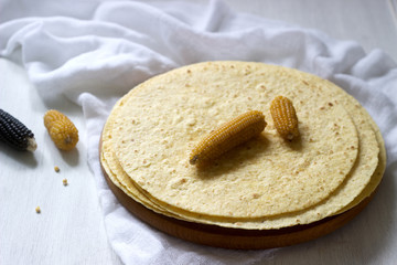 Fototapeta na wymiar A stack of round corn tortillas on a wooden board and corncobs.