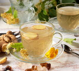 transparent cup of herbal linden tea and pieces of ginger on a white wooden board