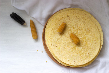 A stack of round corn tortillas on a wooden board and corncobs.